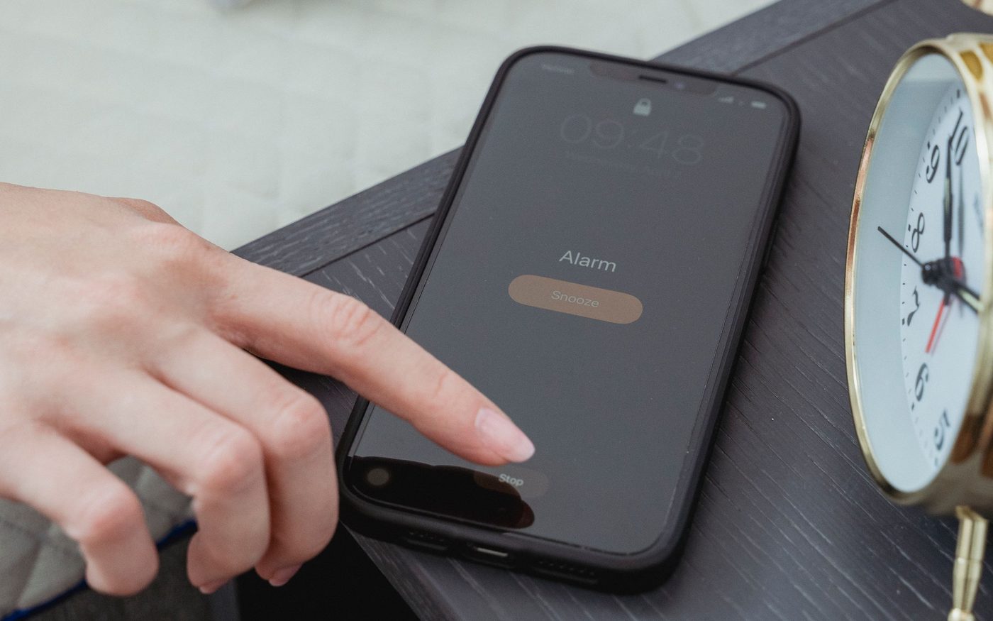 ベッド脇のナイトテーブルで、スマートフォンのアラームを止めようとしている手